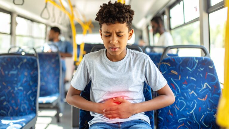 Ein junger Junge mit schmerzverzerrtem Gesichtsausdruck, der in einem Bus Bauchschmerzen hat
