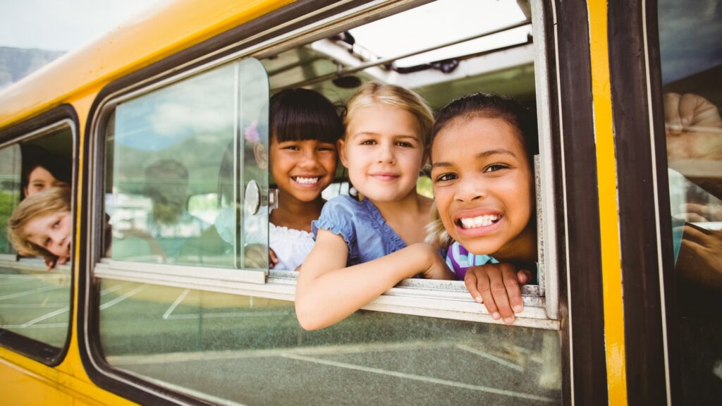 Lächelnde Kinder schauen aus einem Schulbusfenster